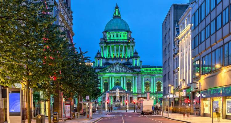 Belfast City Hall illuminated in green during blue hour on an empty street.