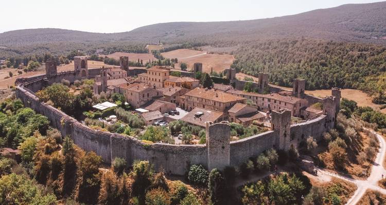 Vue aérienne d'un village médiéval fortifié parfaitement préservé entouré par la campagne toscane.