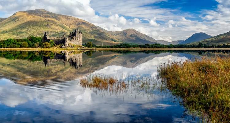 Le château en ruines de Kilchurn se reflétant dans un loch écossais tranquille au milieu des highlands ondulants.