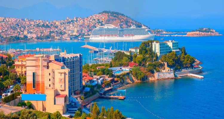 Panoramic view of Kusadasi’s harbour with a large cruise ship, colourful buildings and bright blue Aegean waters.