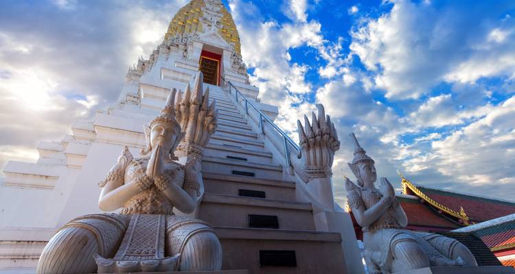 Omhoog kijkend perspectief van een witte Thaise pagode en beschermende standbeelden tegen een gedeeltelijk bewolkte hemel.