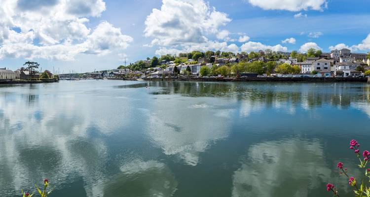 Un estuaire tranquille reflétant une petite ville irlandaise avec des bateaux dispersés et un ciel rempli de nuages.
