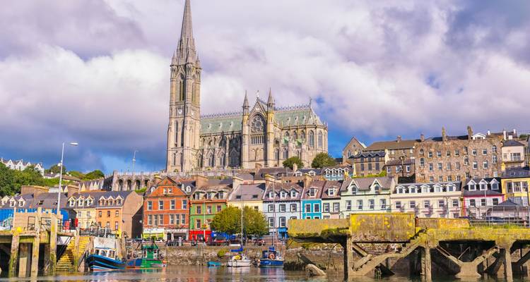 Colorful harbor town of Cobh with St. Colman’s Cathedral towering above row houses and boats.
