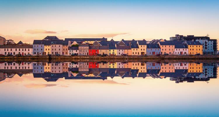 Row of pastel waterfront houses in Galway perfectly mirrored in still evening water.