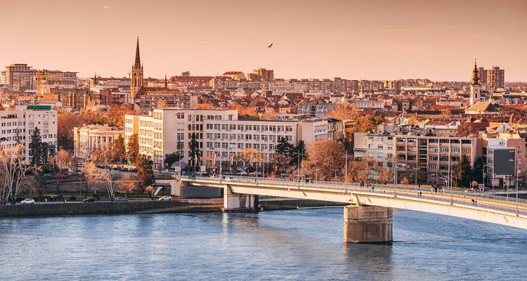 Golden-hour view of Novi Sad with bridge spanning the Danube and city lights.