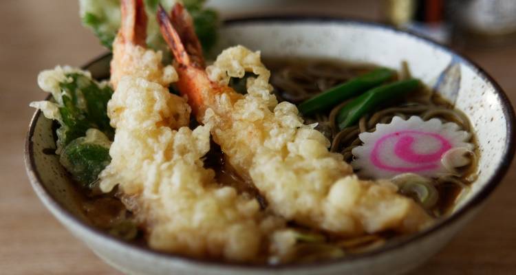 Gros plan d'un bol de nouilles soba aux crevettes tempura avec gâteau de poisson et légumes dans un bouillon.