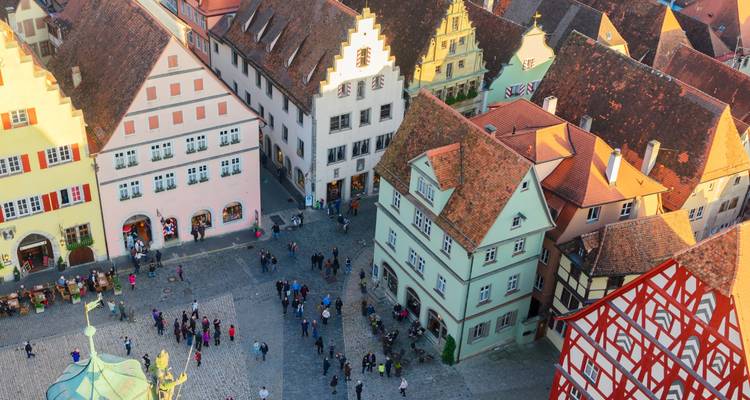 Bird’s-eye view of a medieval town square bustling with tourists among pastel half-timbered houses.