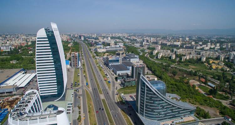 Modern skyline of Sofia with sleek glass towers lining a major boulevard and mountains on the horizon.