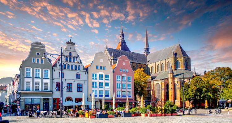Picturesque German market square with colorful gabled facades and gothic church spires at sunrise.