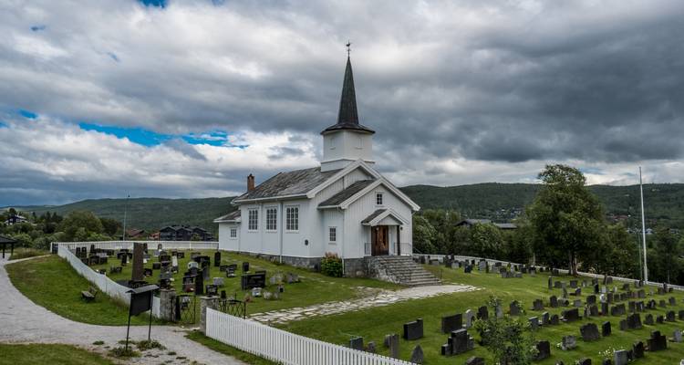 Small white wooden church with steeple overlooking a rural cemetery set against rolling green hills.