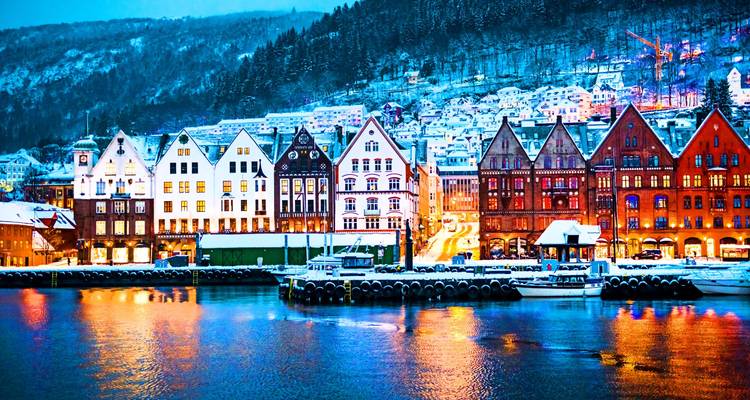 Le quai enneigé de Bryggen avec ses entrepôts en bois aux couleurs vives se reflétant dans les lumières du port en soirée à Bergen.