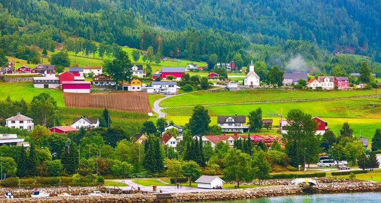 Charmant village rural norvégien avec des maisons colorées, une église et des terres agricoles nichés parmi les collines verdoyantes au bord d'un fjord.