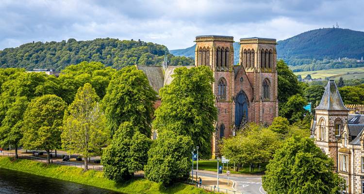 Inverness Cathedral surrounded by lush trees with rolling Scottish hills in the background.