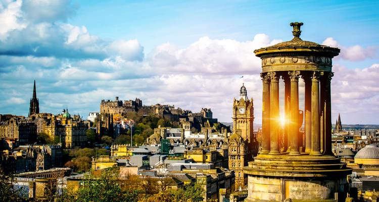 Vue classique depuis Calton Hill avec le Monument de Dugald Stewart et le Château d'Édimbourg baignés par la lumière dorée du soleil au-dessus de la ligne d'horizon de la ville.