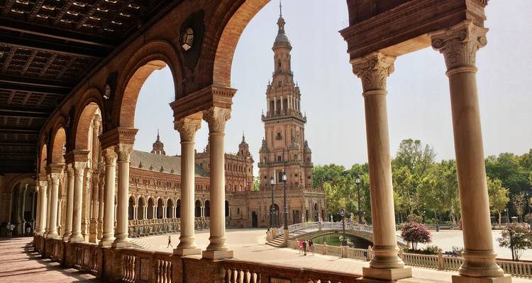 Blick durch Ziegelbogengewölbe auf den kunstvollen Turm der Plaza de España und den Kanal in Sevilla