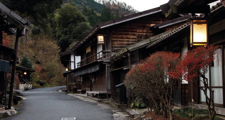 Ruhige traditionelle Holzdorfstraße vor bewaldeten Hügeln unter sanftem Morgenlicht.