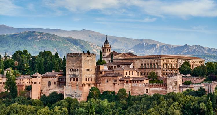 Tagsüber Ansicht des Alhambra-Festungskomplexes, gerahmt von grünen Bäumen und entfernten Bergen.