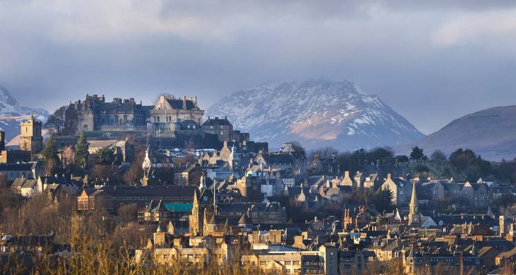 Panoramic morning view of Stirling with Stirling Castle perched above the town and snowy mountains beyond.