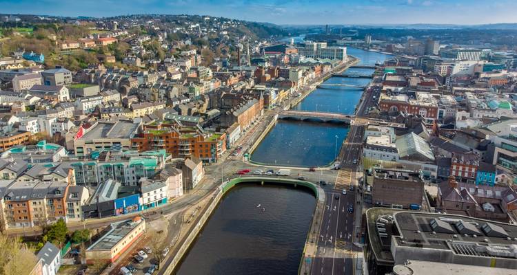 Drone view of Cork city with the River Lee weaving through multiple bridges and colorful buildings.