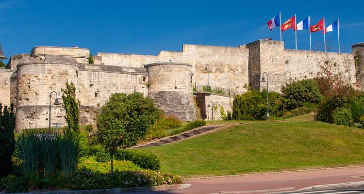 Les remparts de pierre et les drapeaux flottant au-dessus du Château de Caen sous un ciel bleu clair de Normandie.