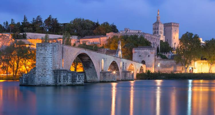 Beleuchtete Pont Saint-Bénézet und Palais des Papes, die sich in der Rhône zur Dämmerung spiegeln.