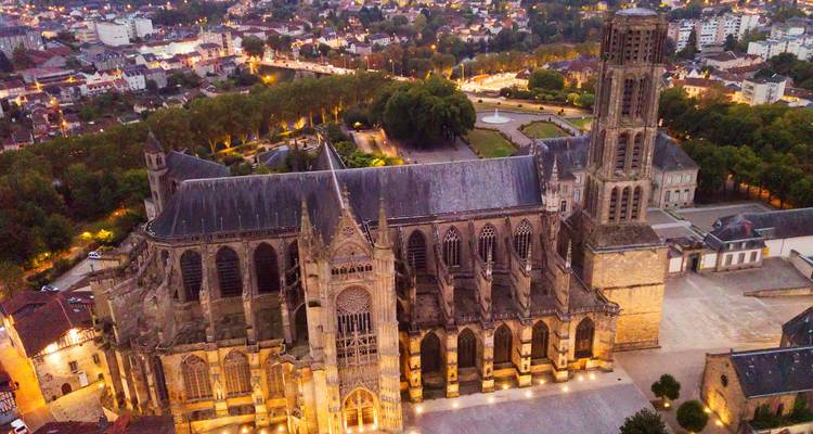 Abendliche Luftaufnahme einer gotischen Kathedrale, die gegen einen Dämmerungshimmel beleuchtet ist, mit umliegenden Stadtlichtern.