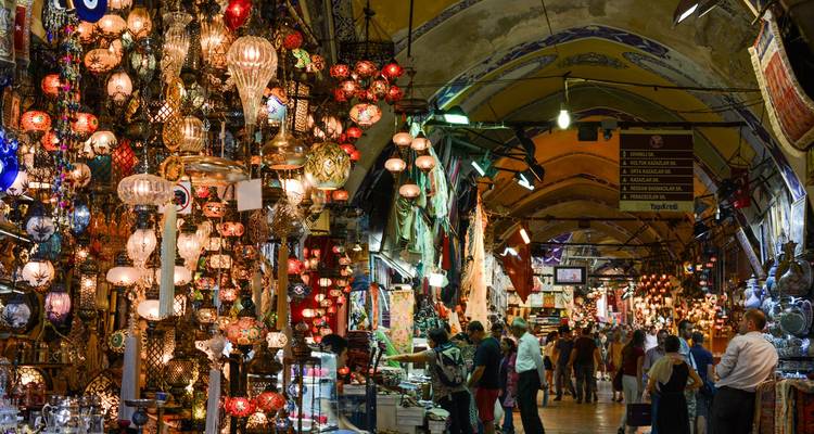 Intérieur animé du Grand Bazar d'Istanbul rempli de lanternes brillantes, de clients et d'étals richement décorés.