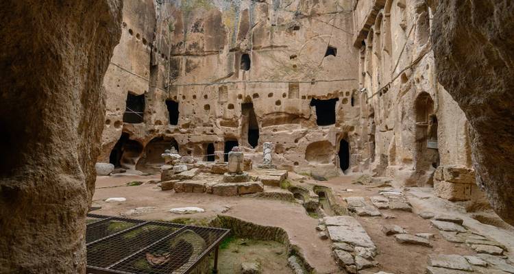 Des chambres et des piliers taillés dans la roche à l'intérieur d'une ancienne ville souterraine avec des artefacts dispersés sur le sol.