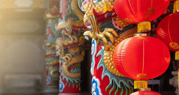 Close view of ornate red lanterns and golden dragon carvings of a Chinese temple with warm sunlight