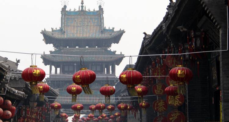 Narrow ancient street in Pingyao decorated with rows of hanging red lanterns and a towering gate in background