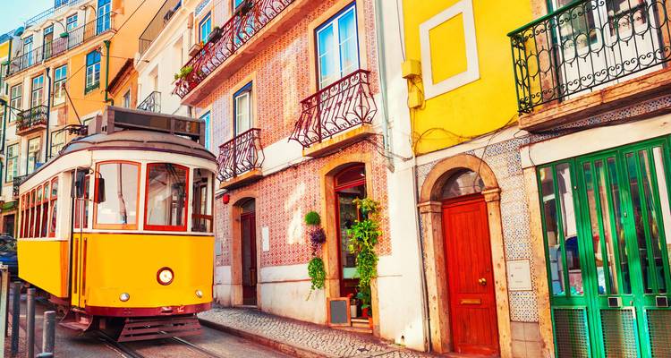 Un tramway jaune classique passant devant des maisons anciennes colorées sur une rue étroite de Lisbonne.