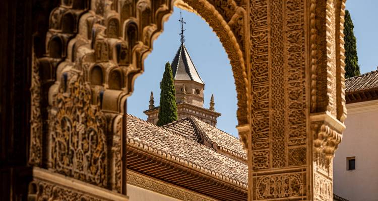 Arc mauresque complexe encadrant un toit carrelé et des cyprès au sein du complexe de l'Alhambra.
