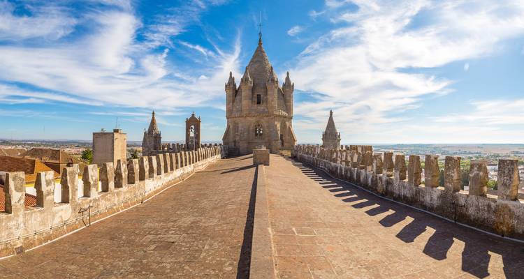 Passerelle sur toit de pierre et clocher de la Cathédrale d'Évora sur fond de ciel dégagé.