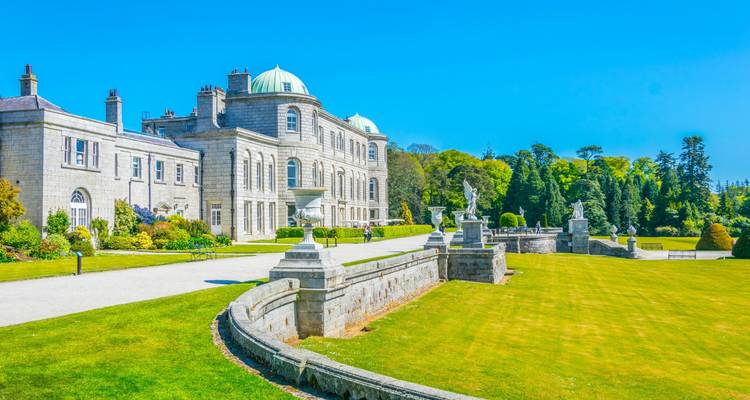 Elegant Georgian mansion of Powerscourt House set amid manicured lawns, statues and bright blue skies.