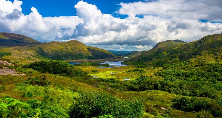 Sweeping vista of lush valleys, lakes and mountains under dramatic white clouds in Killarney National Park.