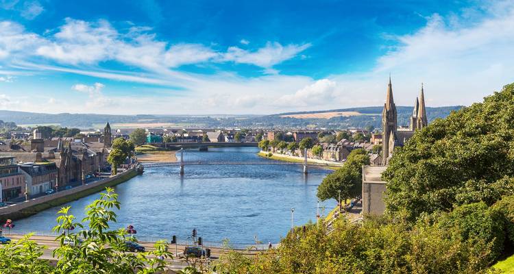 Panoramic view over the River Ness and bridges with Inverness town and distant hills under a clear sky.