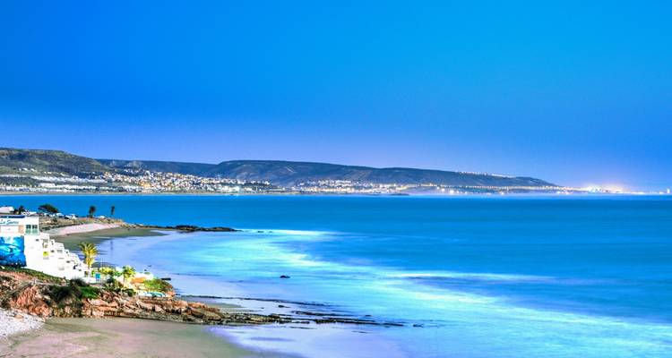 Serene twilight view over Agadir’s long coastline with soft blue hues and distant city lights.
