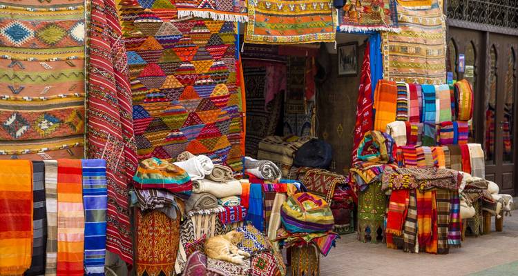 Colourful display of patterned Moroccan carpets and textiles hanging outside a souk stall in Marrakech.