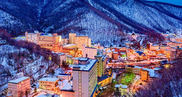 Vallée de montagne couverte de neige parsemée de bâtiments brillamment illuminés d'une ville thermale au crépuscule.