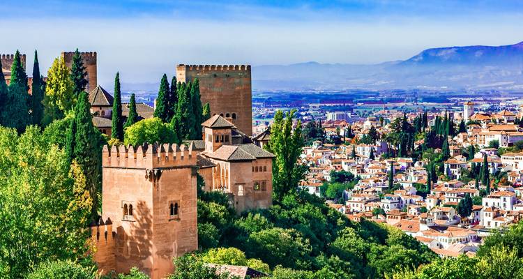 Vue panoramique des fortifications rougeâtres de l'Alhambra entourées de cyprès verts donnant sur la ville en contrebas.