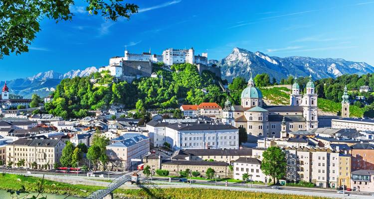 Sprookjesachtig uitzicht op de oude stad Salzburg met de Hohensalzburg Fortress op de achtergrond tegen alpiene pieken en blauwe hemel.