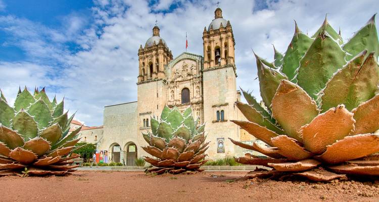 Des plantes d'agave encadrant l'église baroque Santo Domingo sous un ciel partiellement nuageux.