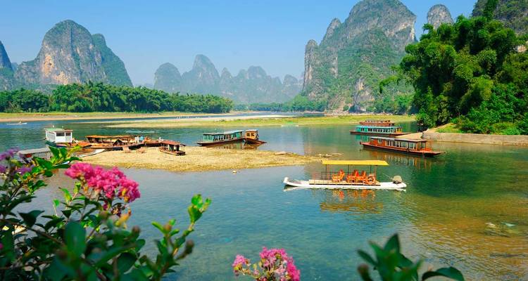 Los botes navegan lentamente por el río Li, de aguas color esmeralda, rodeados de dramáticos picos de karst y flores en flor.