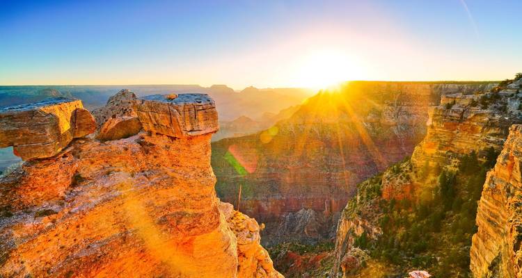 Sunrise illuminates the Grand Canyon’s layered cliffs with golden light and lens flare.