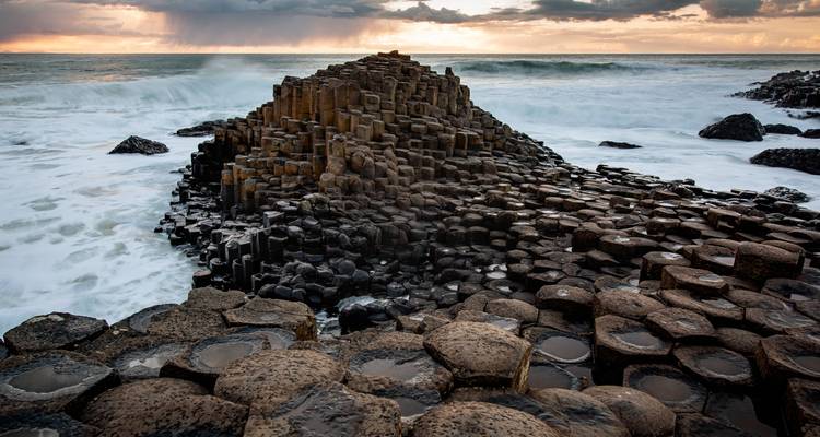 Dramatic basalt columns of the Giant's Causeway with waves crashing under a moody sunset sky.