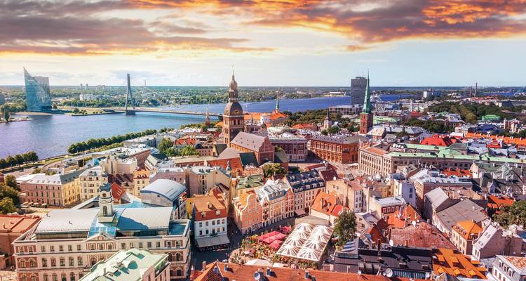Panorama dramatique du coucher de soleil à Riga avec le fleuve Daugava, les ponts et l'horizon historique sous des nuages enflammés.