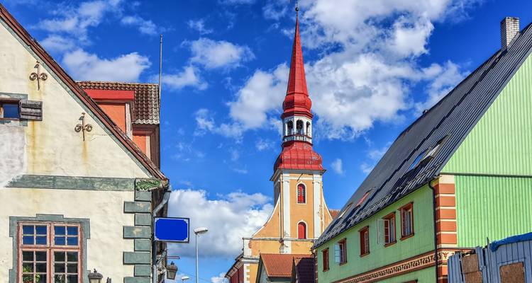 Des maisons en bois peintes de couleurs vives et une haute église au clocher rouge se dressent contre un ciel parsemé de nuages cotonneux à Parnu.
