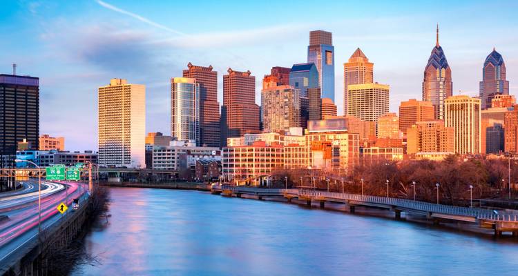 Philadelphia skyline die gloeit in warm gouden-uurtjeslicht langs de Schuylkill River met reflecties op het water.