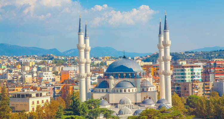 Grand Namazgâ Mosque with twin minarets towering over Tirana's modern skyline and mountain backdrop.