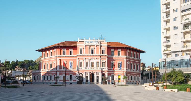 Restored pink neoclassical government building standing in a spacious modern square under clear skies.